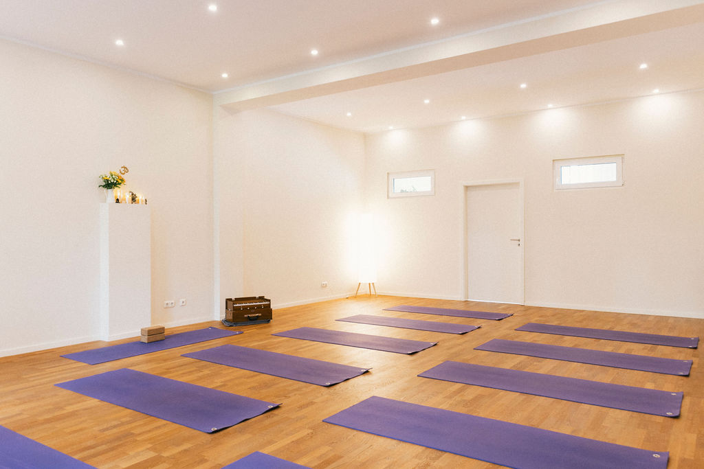 Großer, heller Yogaraum, in dem Yogamatten ausgelegt sind auf einem Holzboden.